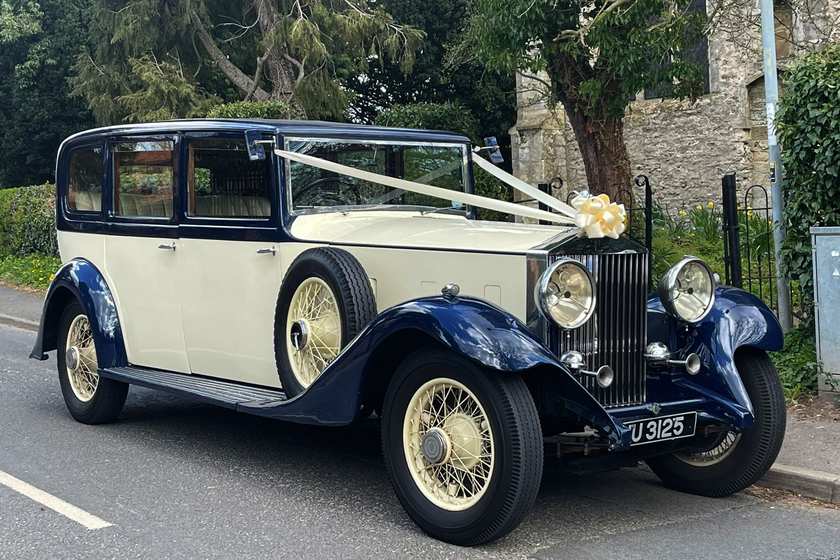 A navy and ivory vintage Rolls Royce with ivory wire wheels and ivory ribbons across the bonnet.