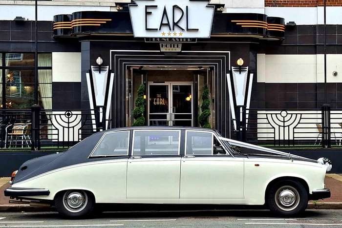 A Daimler limousine in black and Old English White, dressed with ribbons, outside an art deco hotel entrance.