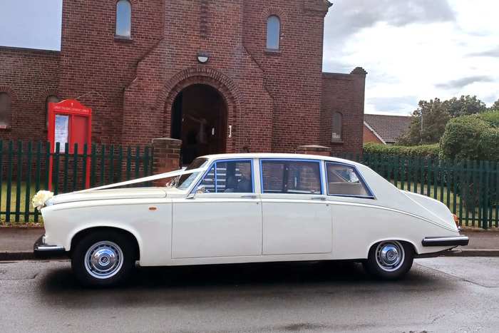 An ivory Daimler limousine with ribbons, parked outside a red brick church.