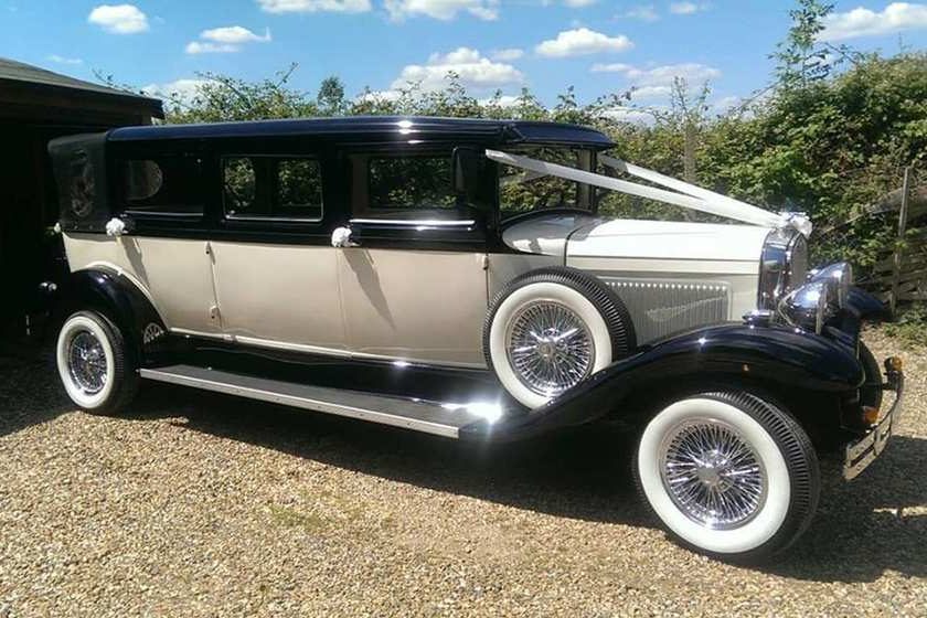 A long ivory and black vintage-style Ford Bramwith limousine with whitewall tyres and chrome wire wheels.