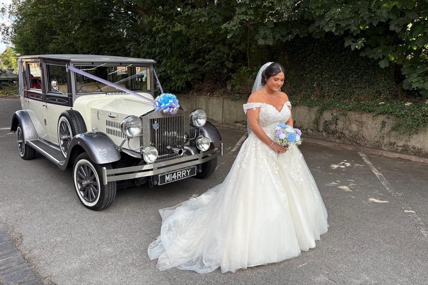 A bride holding a blue and lilac bouquet beside an ivory and silver Imperial Viscount dressed with lilac ribbons and a blue bow.